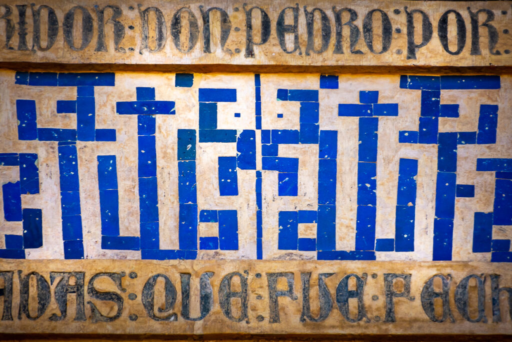 Dettaglio degli azulejos blu e bianchi sulla facciata del Palacio de Pedro I, con scrittura cufica quadrata e iscrizione superiore.
