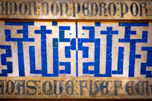 Dettaglio degli azulejos blu e bianchi sulla facciata del Palacio de Pedro I, con scrittura cufica quadrata e iscrizione superiore.